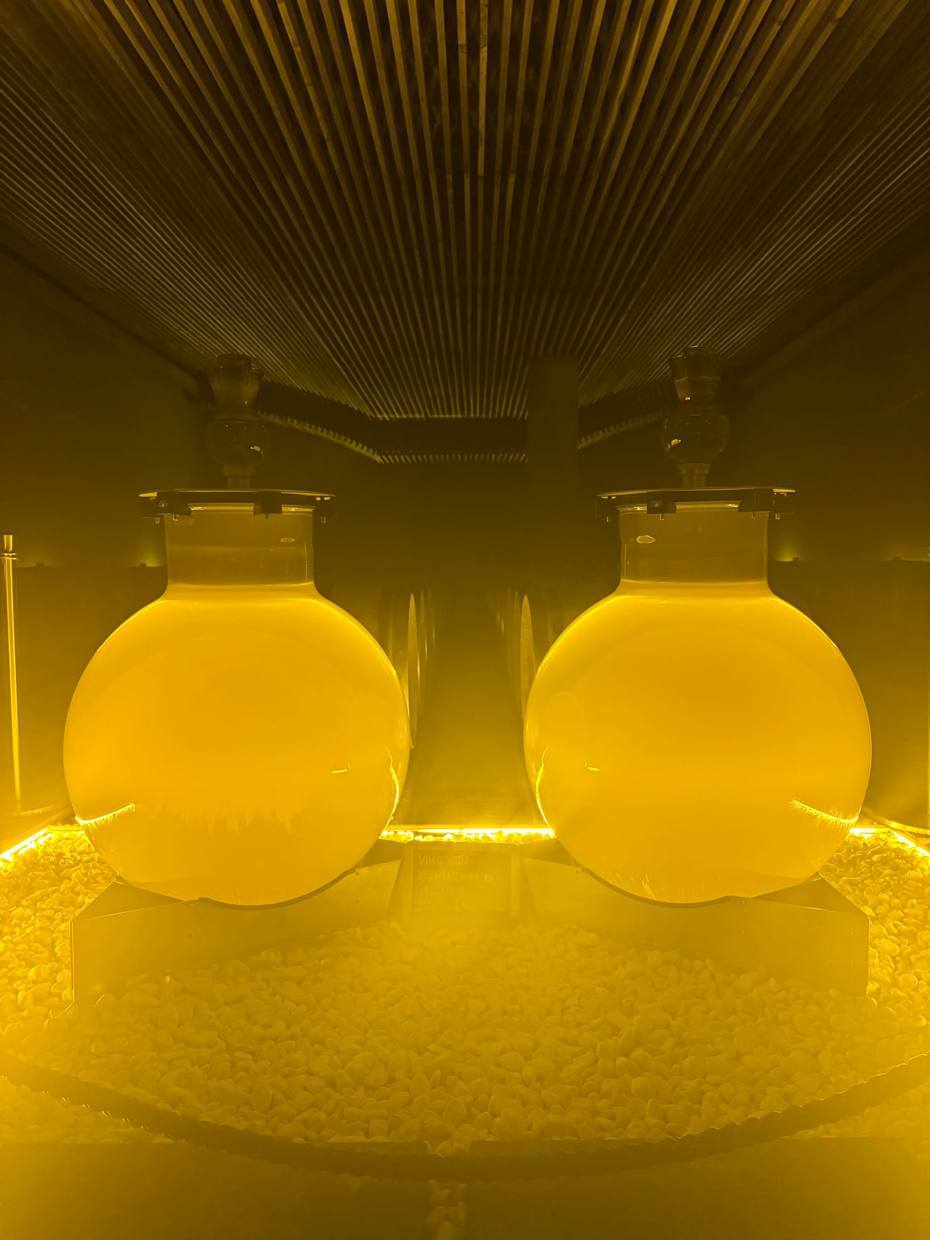 Two round glass wine vessels glowing gold in a dark installation