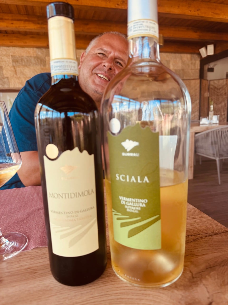 Yanni smiling behind bottles of Montidimola and Sciala Vermentino di Gallura