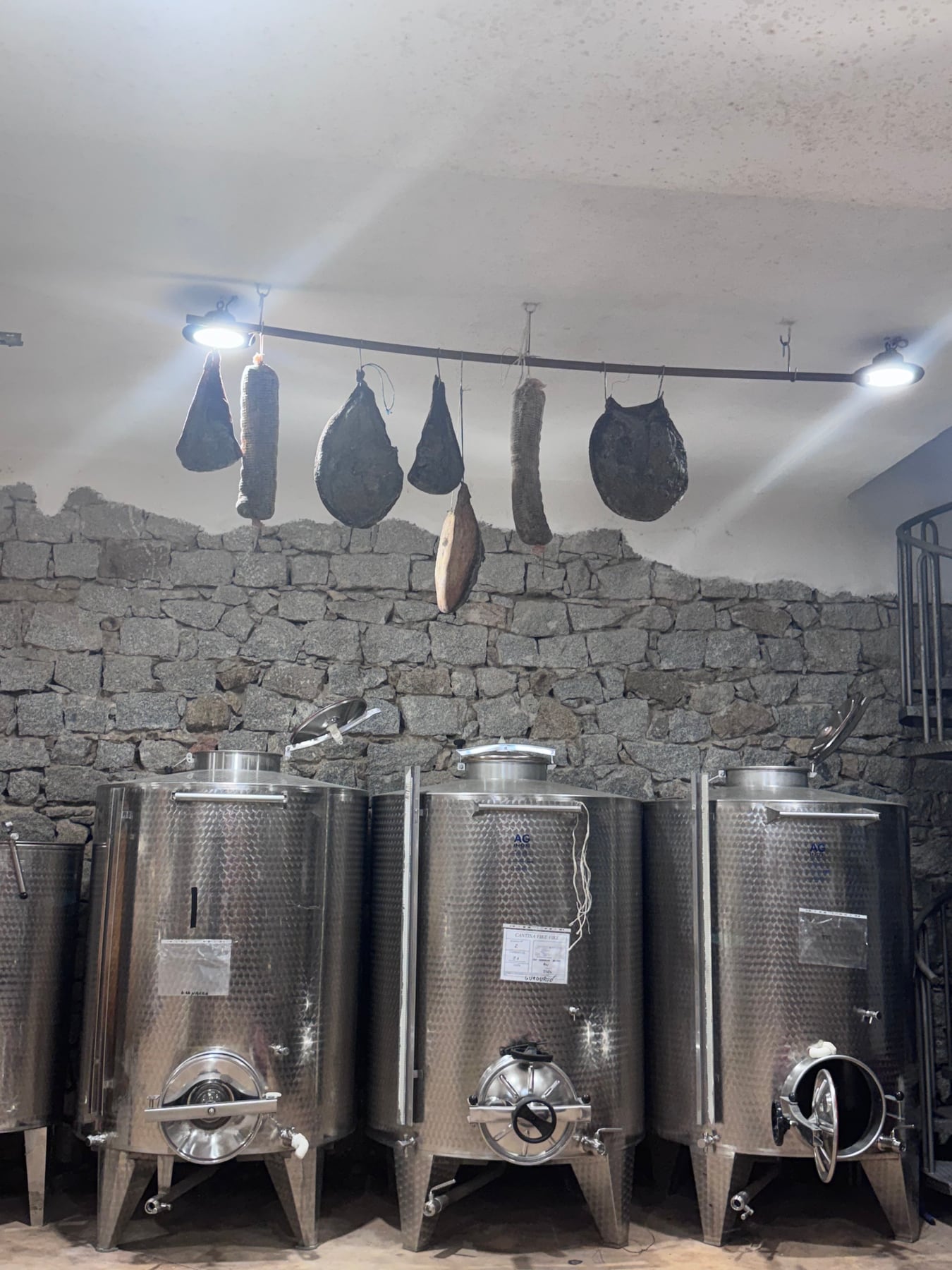 Traditional cured foods hanging above stainless steel cellar tanks