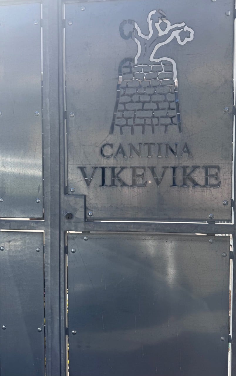 Metal gate bearing the Cantina Vike Vike name and tree-topped stone tower mark